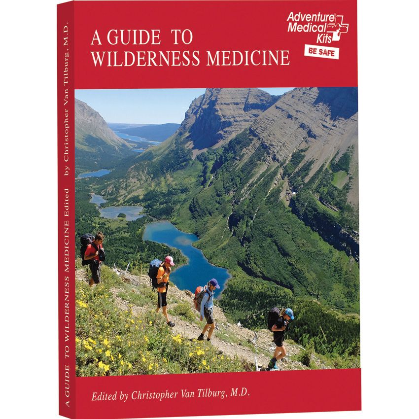 A Guide to Wilderness Medicine book cover and spine, featuring a red header and footer with white title text and a central landscape photo of mountain climbers overlooking blue lakes and green valleys. The Adventure Medical Kits Be Safe logo appears in the top right.