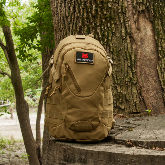 Tan tactical backpack with a brand logo on a tree stump in a forest setting
