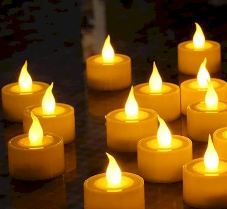 Multiple small candles with glowing flames on a reflective surface.